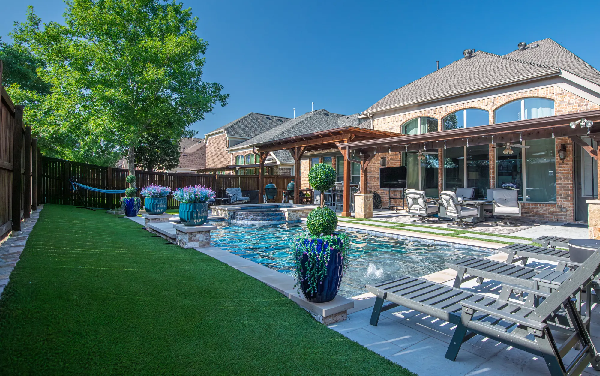 Backyard with artificial turf lawn around a pool and covered patio