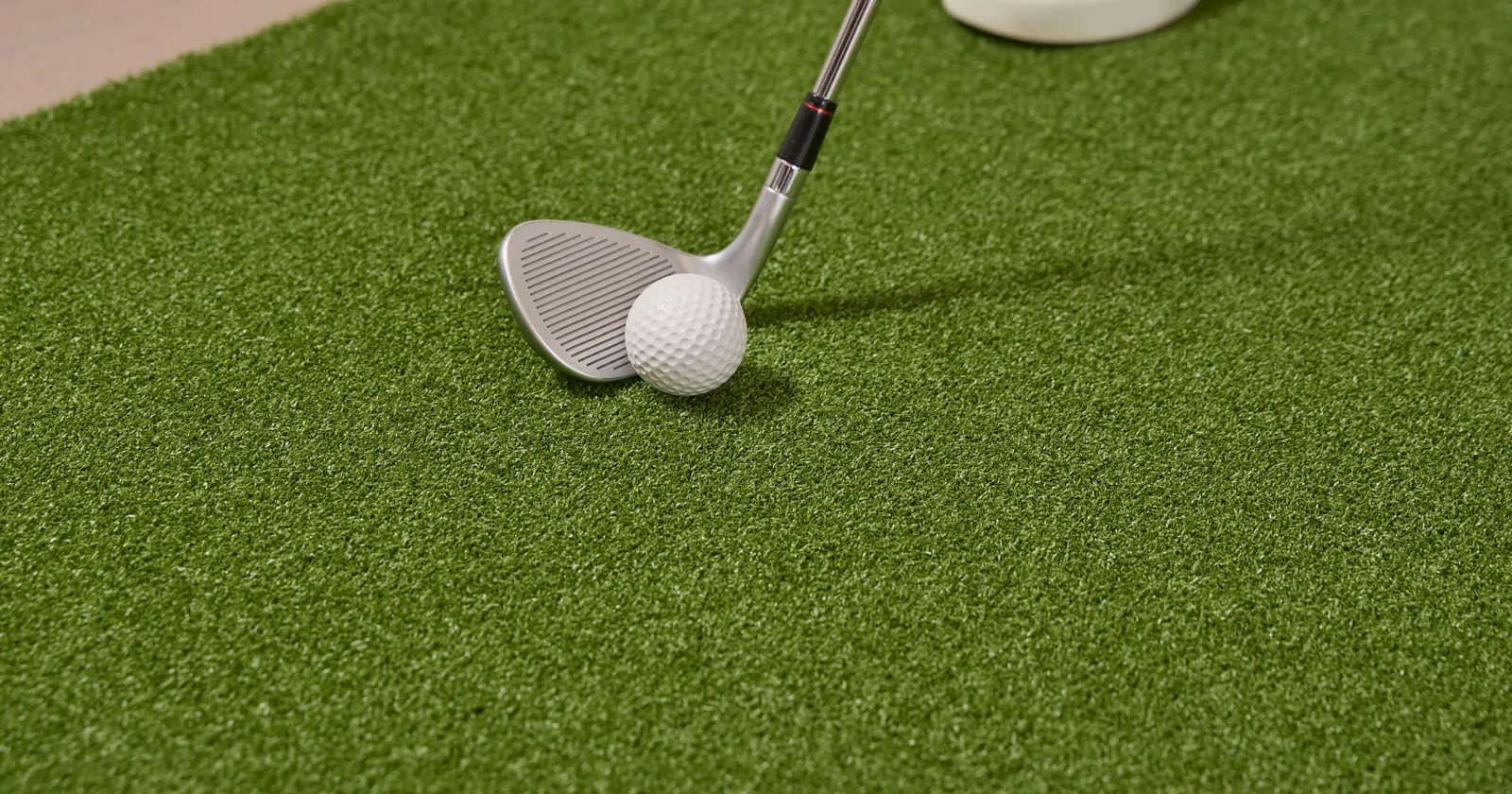 Wedge set up behind a golf ball on artificial turf fringe